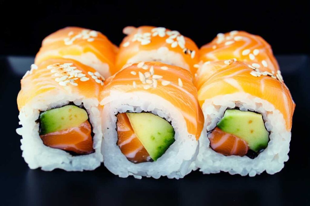 Close-up of freshly prepared Alaskan Roll sushi with salmon, avocado, and rice, garnished with sesame seeds.