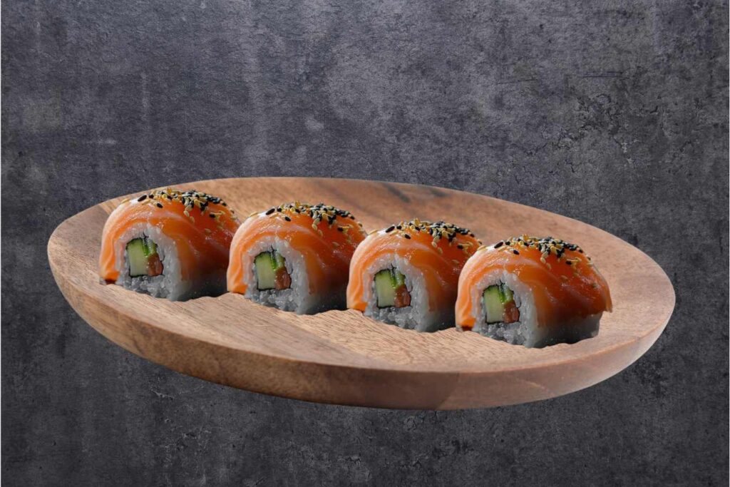 Four pieces of Alaska Roll sushi with salmon, cucumber, and rice, served on a wooden plate against a dark background.