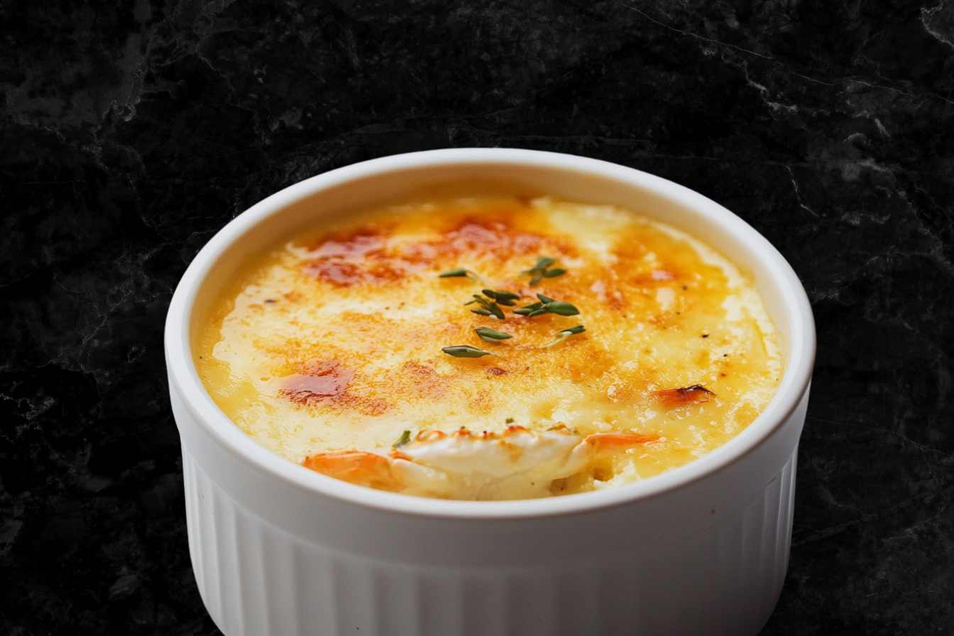 A creamy Crab Brulee Recipe in a white ramekin, topped with a golden caramelized crust and garnished with fresh thyme leaves.