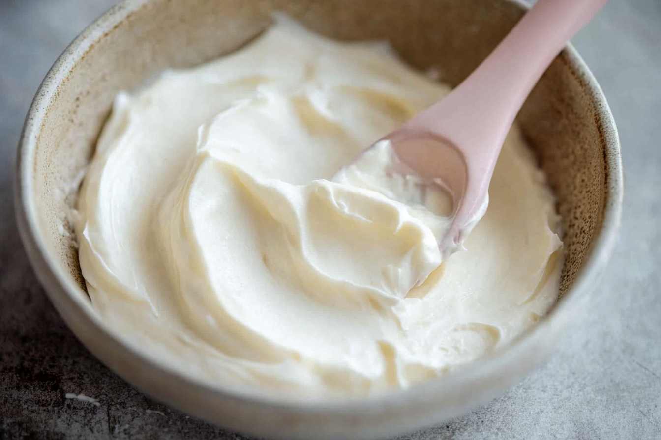 A bowl of smooth and creamy cream cheese filling with a pink spatula resting in it, ready for use in desserts or baked goods.