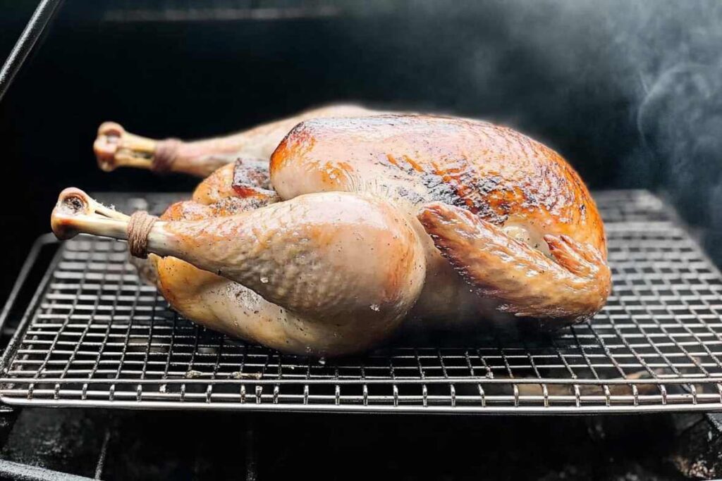 Whole smoked turkey cooking on a grill rack with visible smoke enhancing its golden-brown crust.