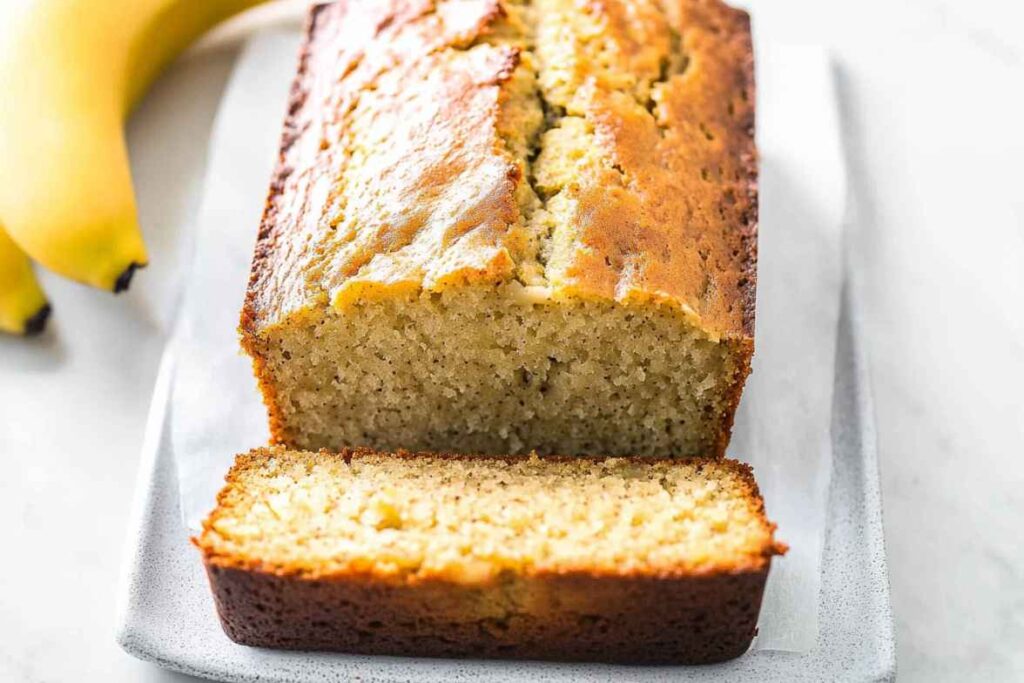 A freshly baked banana bread loaf with a golden crust, sliced to reveal its moist interior.