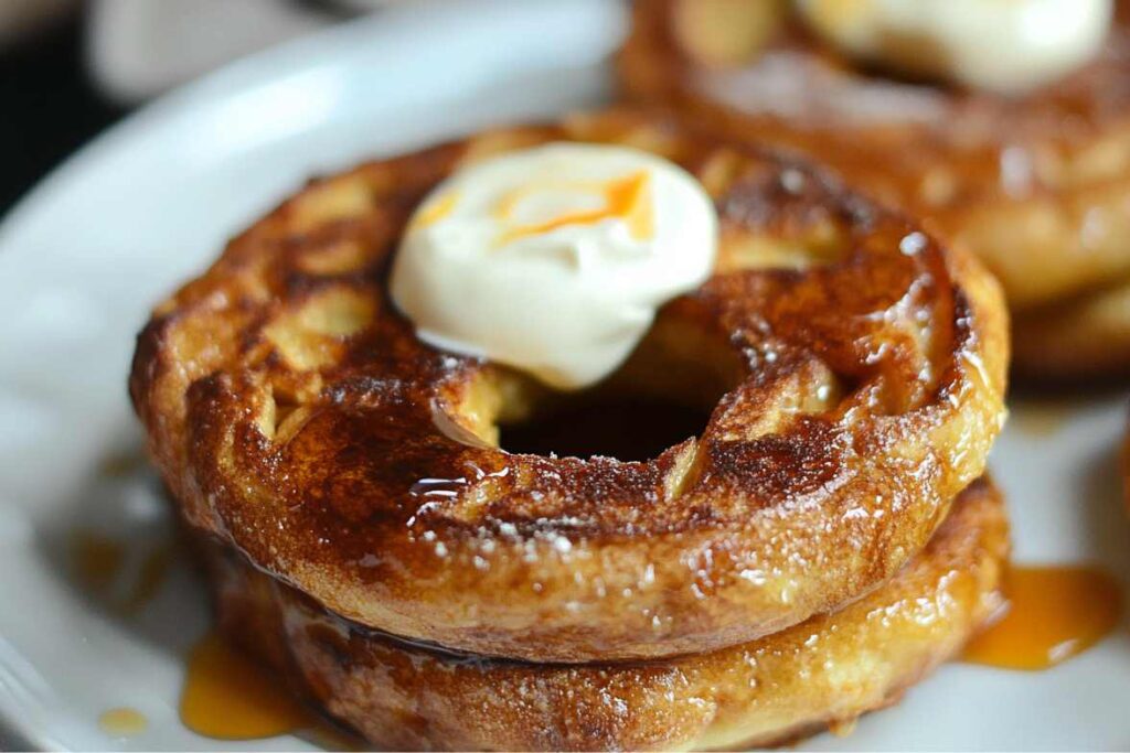 Stacked French Toast Bagels topped with butter and drizzled with maple syrup on a white plate.