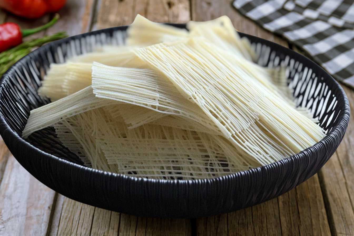 A black bowl filled with neatly arranged bundles of rare, thin spaghetti on a rustic wooden table.