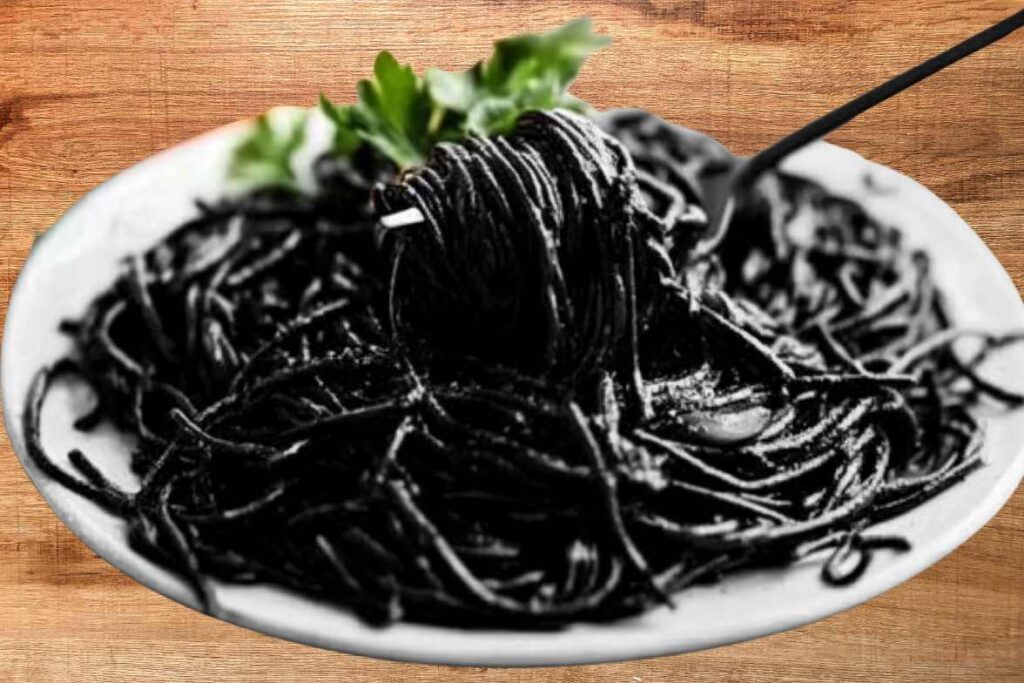 A plate of squid ink spaghetti with a dark, rich coating, garnished with fresh parsley and served on a wooden table.