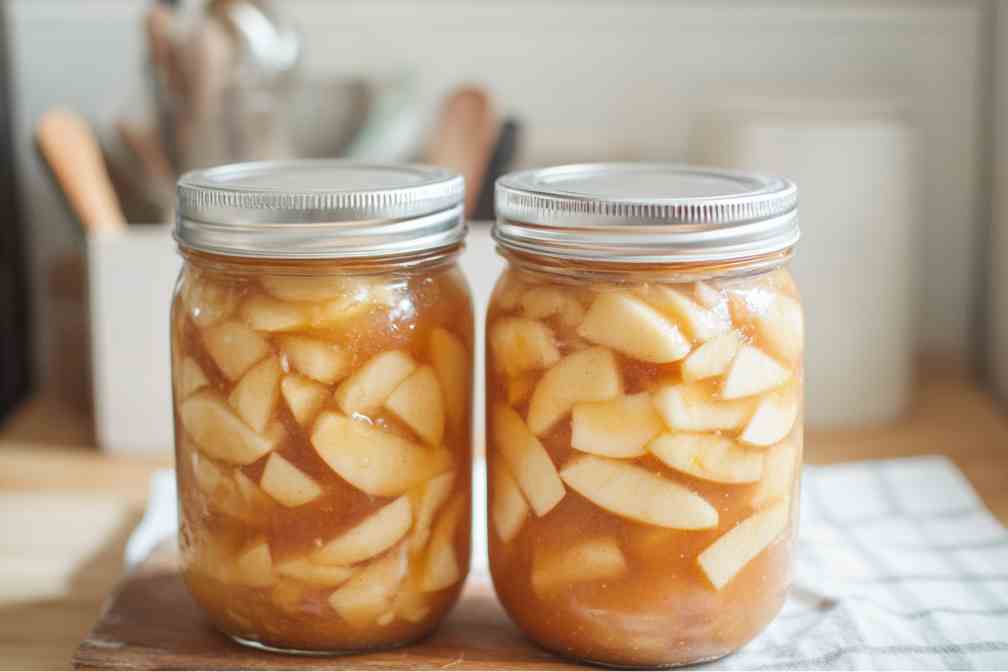 Two mason jars filled with Homemade Apple Pie Filling, featuring tender apple slices coated in a rich, cinnamon-spiced syrup.