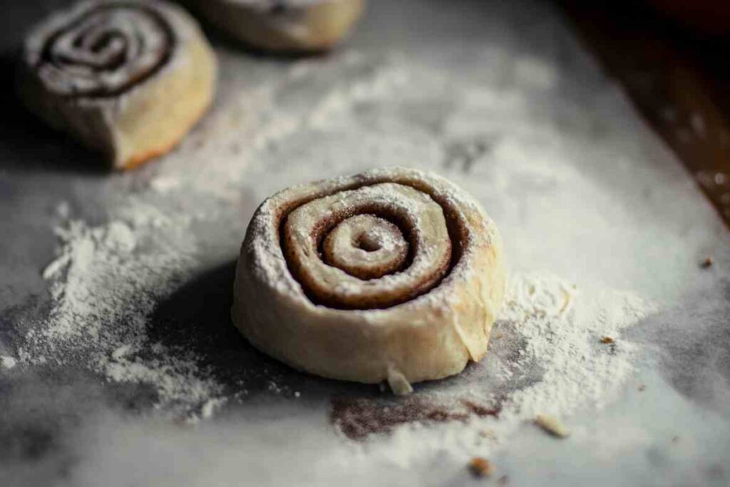 A raw cinnamon roll dusted with flour, ready to be baked.