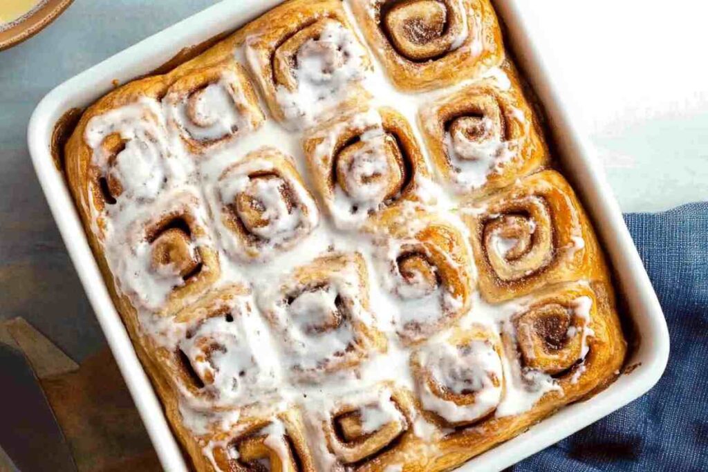 Freshly baked cinnamon rolls topped with creamy icing in a white baking dish.