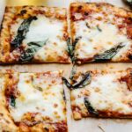 Lavash bread pizza topped with melted cheese and fresh basil leaves, cut into four squares.