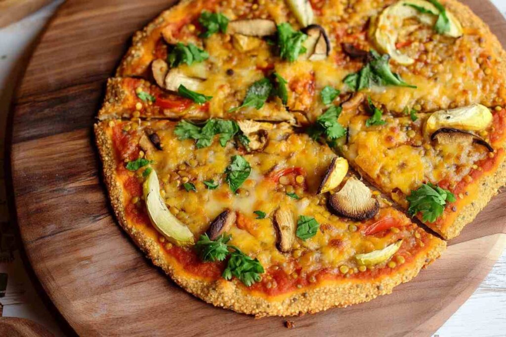 Vegetable-topped pizza with a golden lentil crust garnished with fresh cilantro on a wooden serving board.