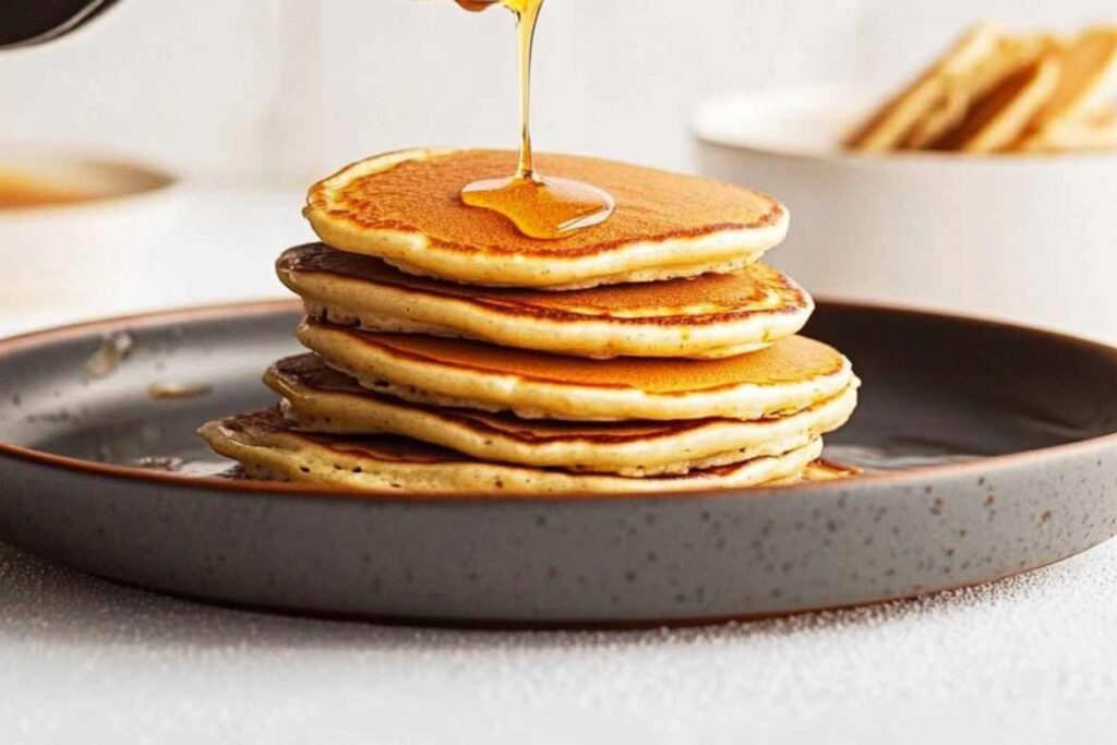 Stack of golden pancakes being drizzled with honey on a rustic plate.