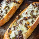 Freshly baked Philly cheesesteak bread with melted cheese, seasoned steak, and peppers on a baking sheet.