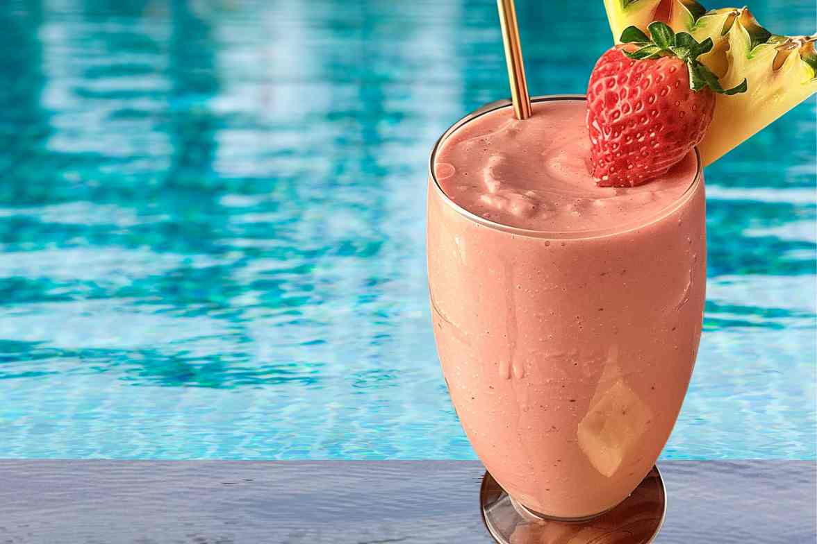 A creamy Bahama Mama Tropical Smoothie served in a chilled glass, garnished with a fresh strawberry and pineapple slice, set against a refreshing poolside backdrop.