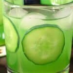 A close-up of a refreshing cucumber mocktail served in a glass filled with ice cubes and thin cucumber slices, with a fizzy texture and a vibrant green hue.