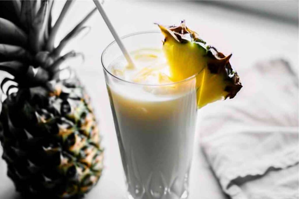 Refreshing piña colada smoothie served in a tall glass with a pineapple garnish.